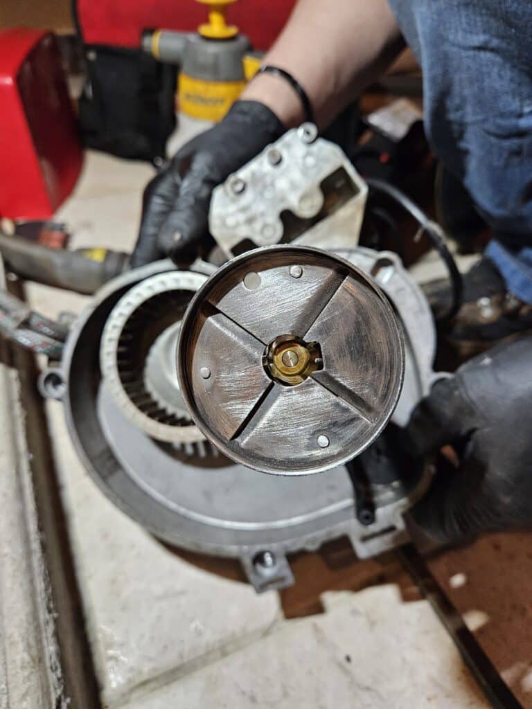 Gros plan sur un brûleur fioul démonté, avec un technicien portant des gants noirs manipulant la tête du brûleur